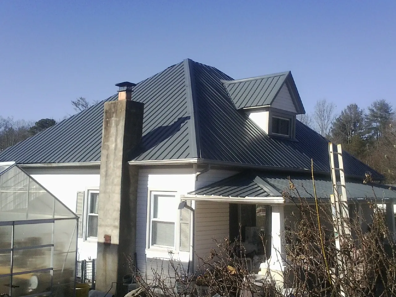 Dark blue standing seam metal roof on a white farmhouse with dormer — Slate & Tile Roof Repair by Roofing Brothers in Tyler Hill