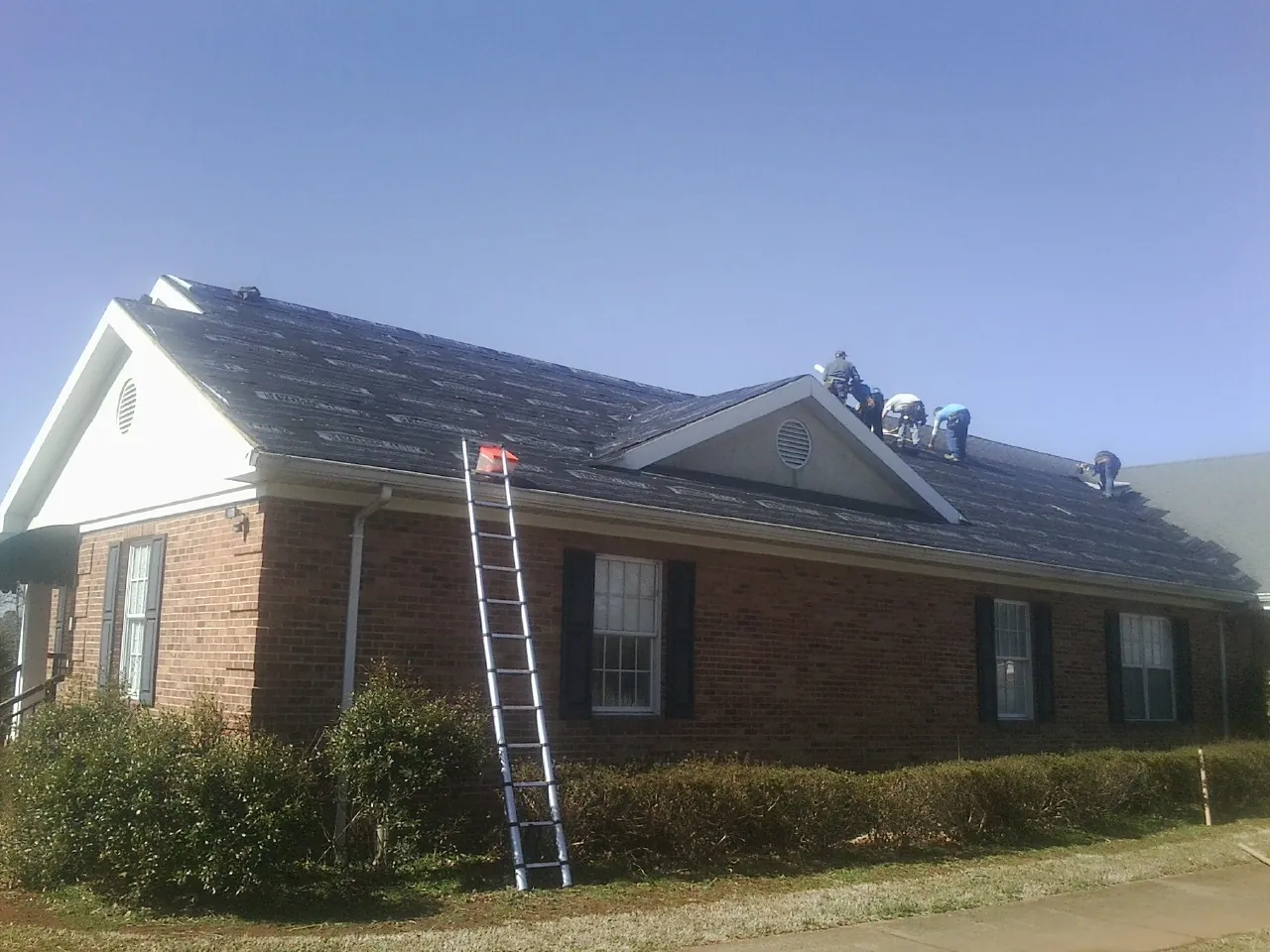 Crew tearing shingles off a brick ranch roof with a ladder set — Emergency Roof Repair work by our crew in Tyler Hill
