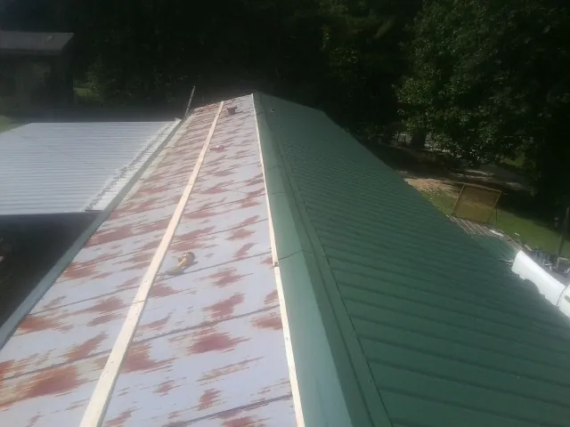 Old rusted panels beside newly installed green metal roofing — Wind Damage Roof Repair by Roofing Brothers in Tyler Hill