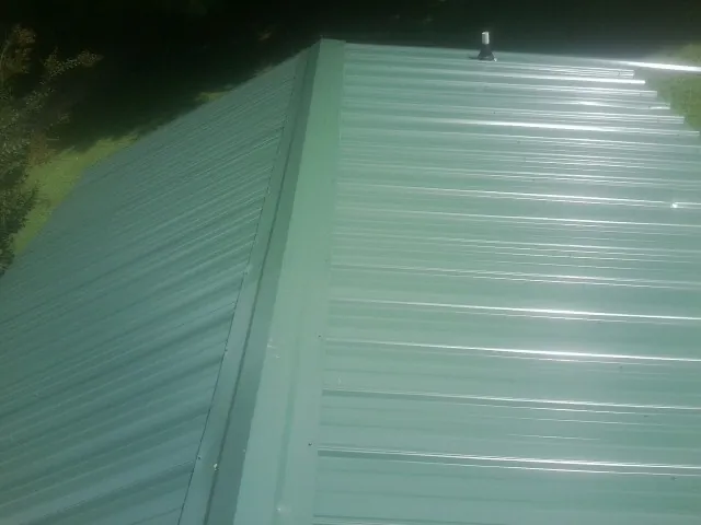 New green metal panels meeting at the ridge of a roof — Flat Roof Repair work by our crew in Tyler Hill