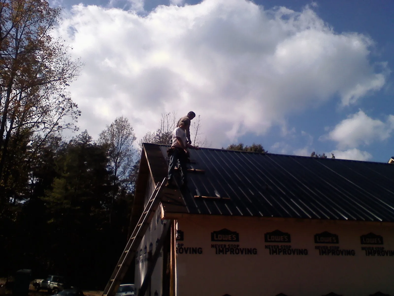 Roofer fastening dark metal panels high against a cloudy sky, from a Roof Inspection job in Tyler Hill