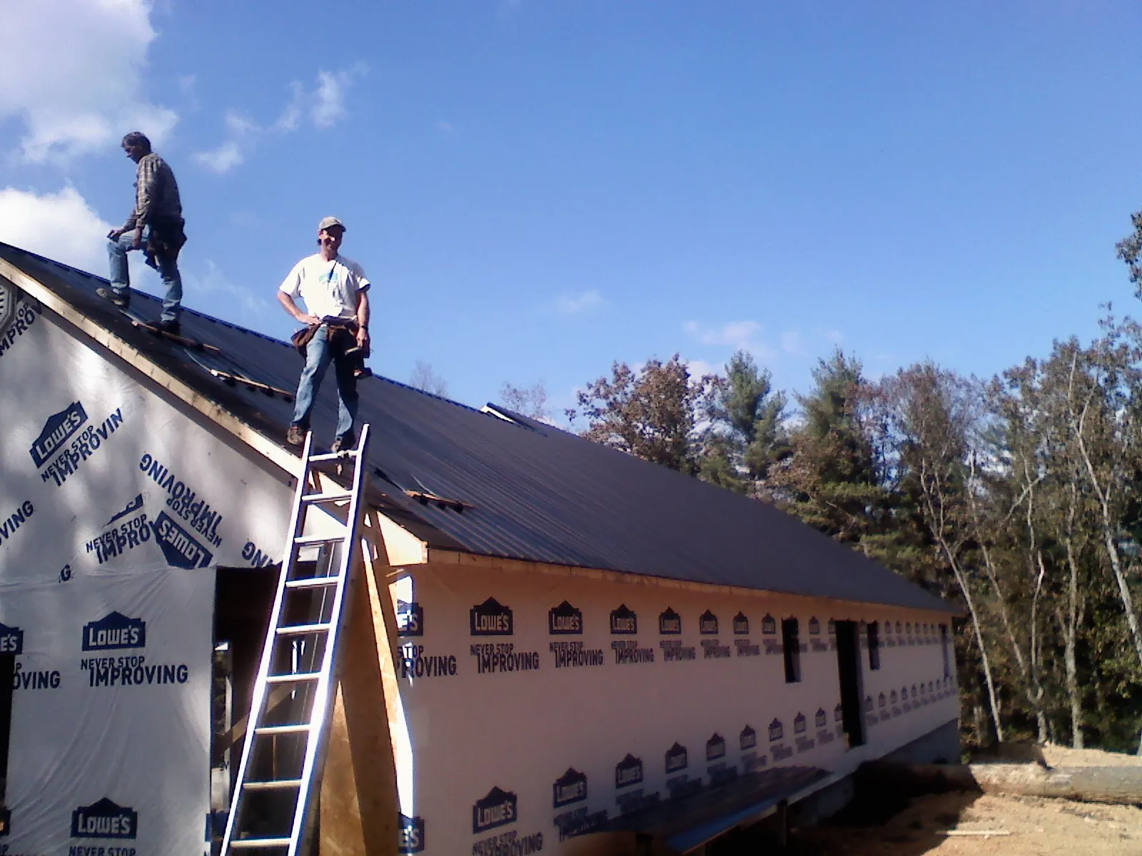 Two roofers standing on a long dark metal roof over a wrapped building in Tyler Hill