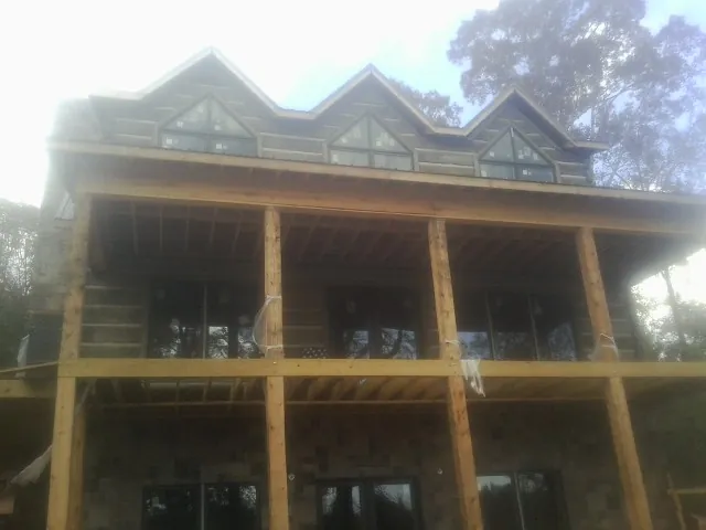 Dormers and porch framing on a large log home under construction — Roof Coating work by our crew in Tyler Hill