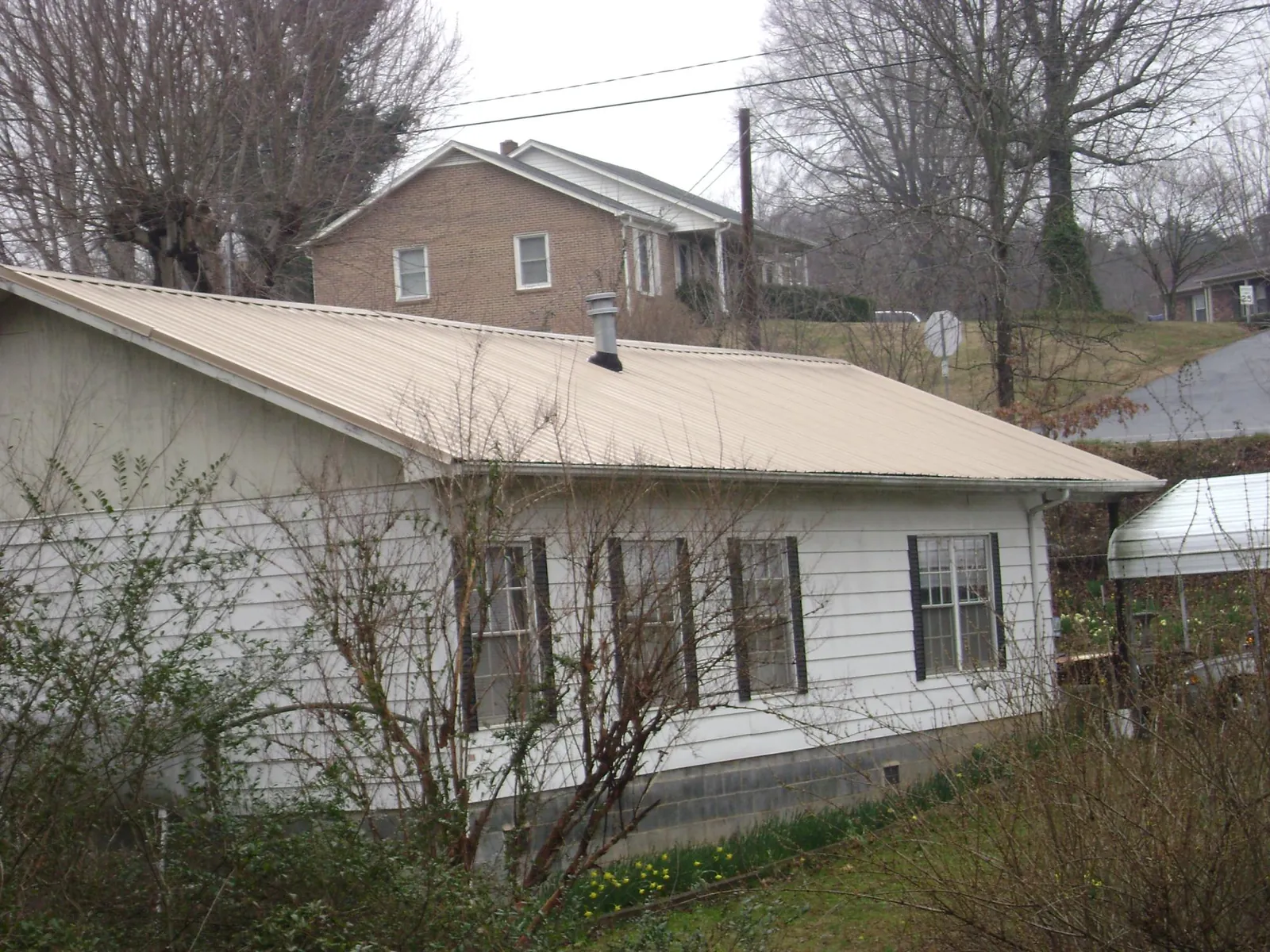 Tan metal roof on a white sided house set into a hillside — Commercial Roofing by Roofing Brothers in Tyler Hill