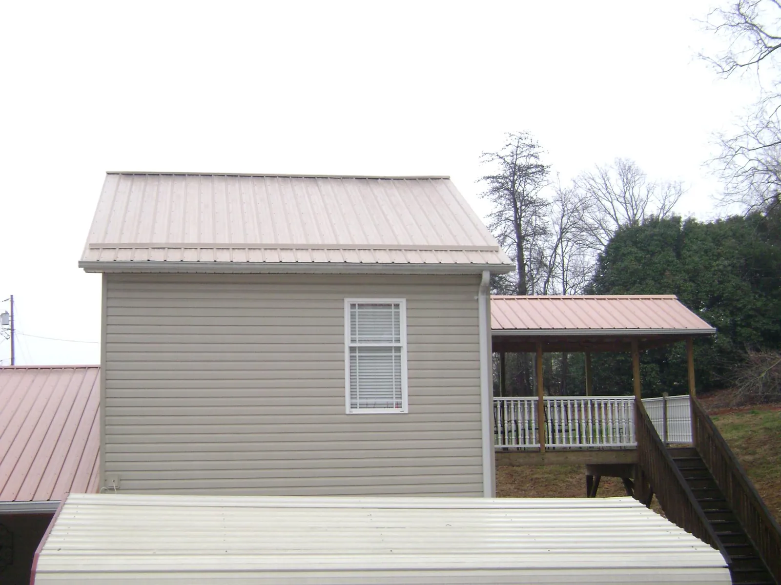 Tan metal roofs on a two story addition and attached porch, from a Roof Replacement job in Tyler Hill