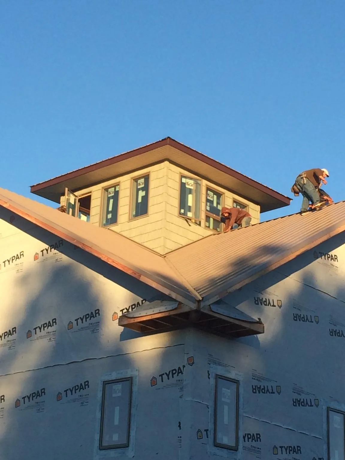 Roofers working around a rooftop cupola on a new metal roof at sunset — Roof Waterproofing in Tyler Hill by Roofing Brothers